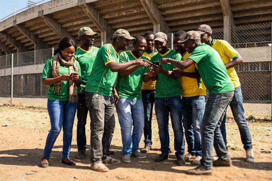 Zimbabwean football supporters outside a stadium checking their phones